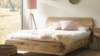 Casa Bella Furniture image of a bedroom with a wooden bedframe, a wool throw, a pink freestanding lamp, beige walls, and glass doors to the left