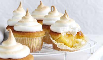Five lemon meringue cupcakes on a cooling rack with the front one open to show the lemon curd filling