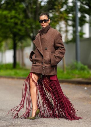 Livia Nunes Marques wears black sunglasses, dark brown oversized belted Ferragamo jacket, dark red marron tassel Ferragamo maxi dress, dark green pointed toe Ferragamo leather heels, outside Ferragamo, during the Milan Fashion Week Spring/Summer 2024-2025 on September 21, 2024 in Milan, Italy.