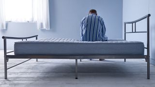 A man sits with his back to the camera on an old, sagging mattress