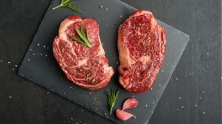 Raw steaks on charcoal board covered with salt and rosemary