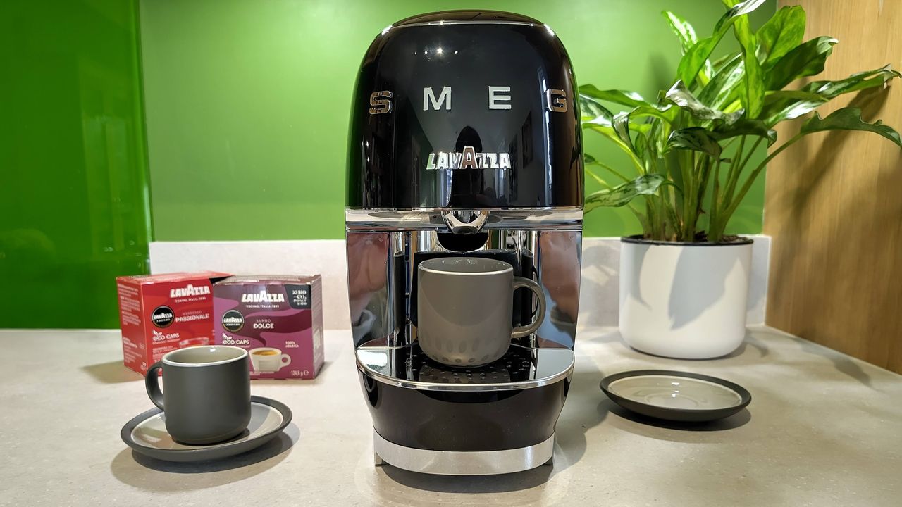 Lavazza A Modo Mio Smeg coffee maker on kitchen counter with espresso cups, box of coffee pods, and plant