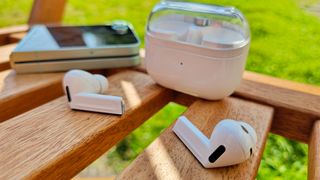 Samsung Galaxy Buds 3 Pro in-ear headphones on wooden bench next to case and Samsung phone