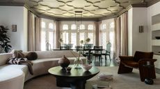 Gothic living room with grand windows and molding on the ceiling, boucle curved sofa, wood dining table, curved wood table, velvet armchair