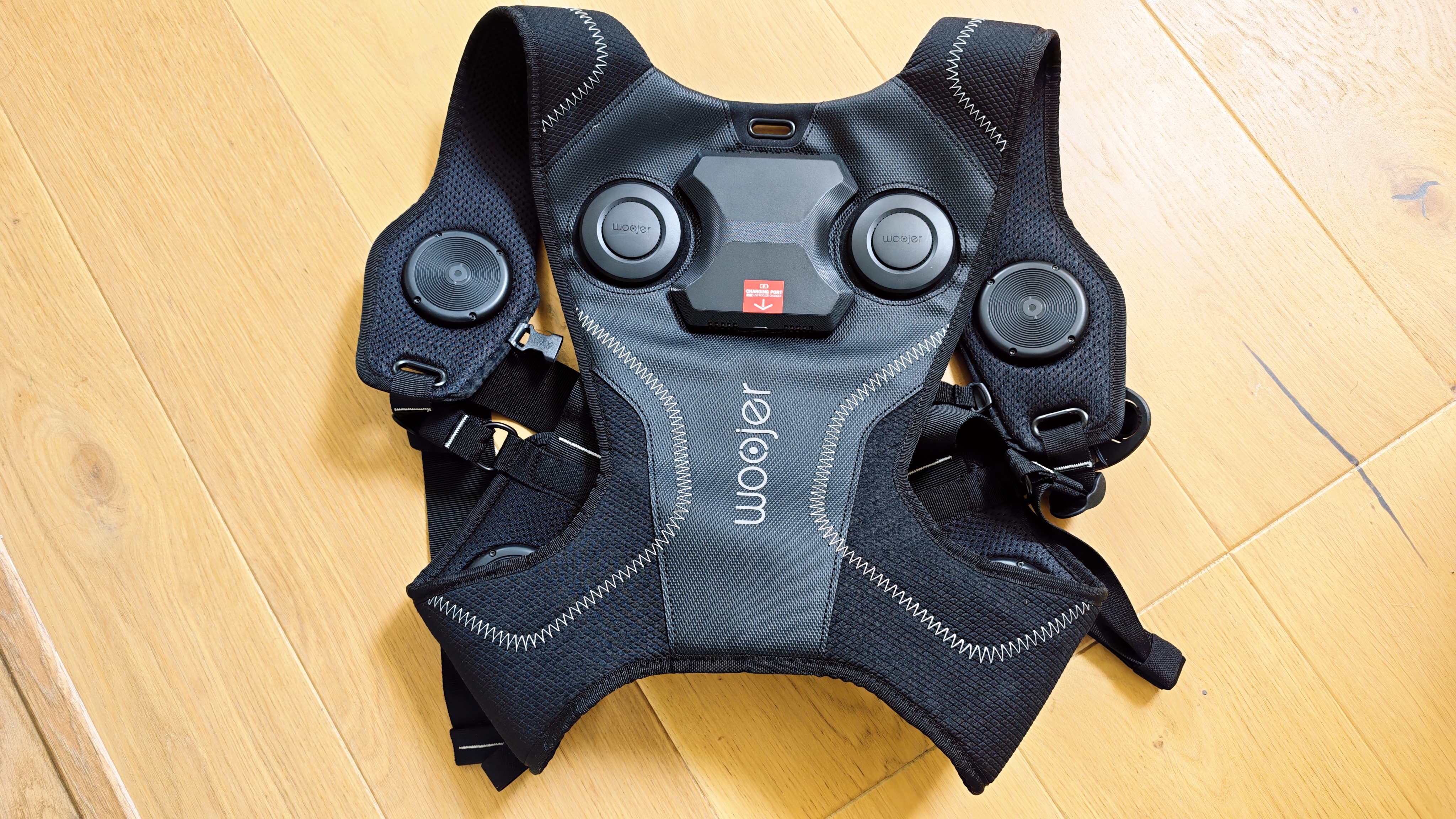 A black Woojer Vest 4 on a wooden floor