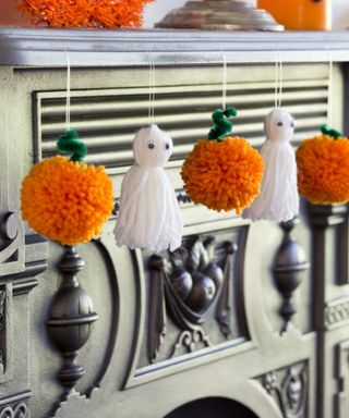 Craft projects for Halloween. Orange handmade Pom-pom pumpkins and tassel ghosts hanging from a mantlepiece.