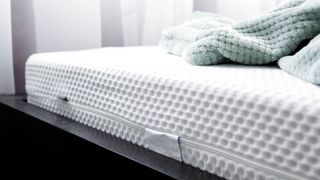 A white memory foam mattress without fiberglass placed on a black bed frame