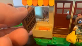 A hand pulls off a secret lid in the Lego Nook's Cranny & Rosie's House set