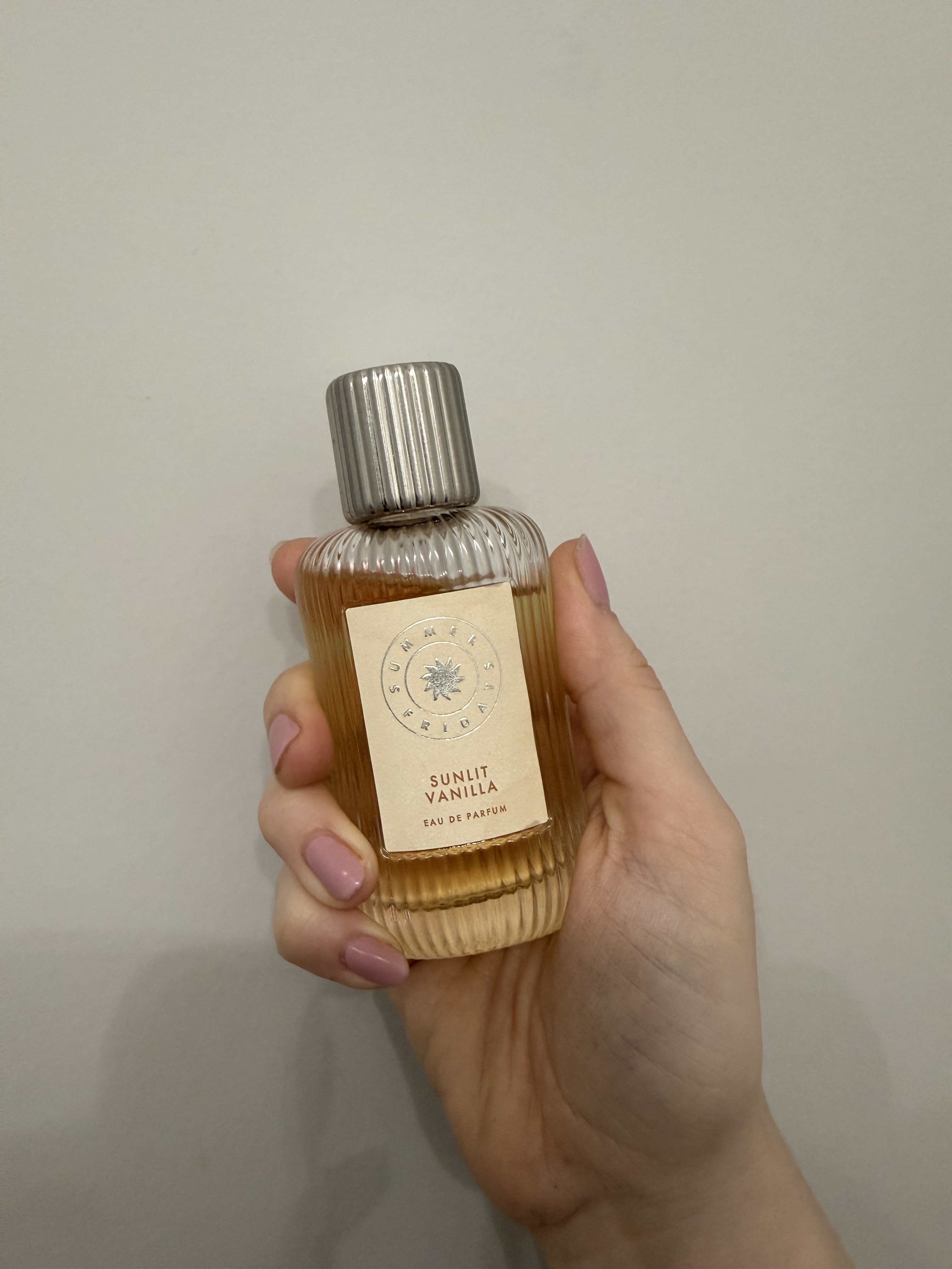 hand holding up summer fridays perfume bottle against grey wall