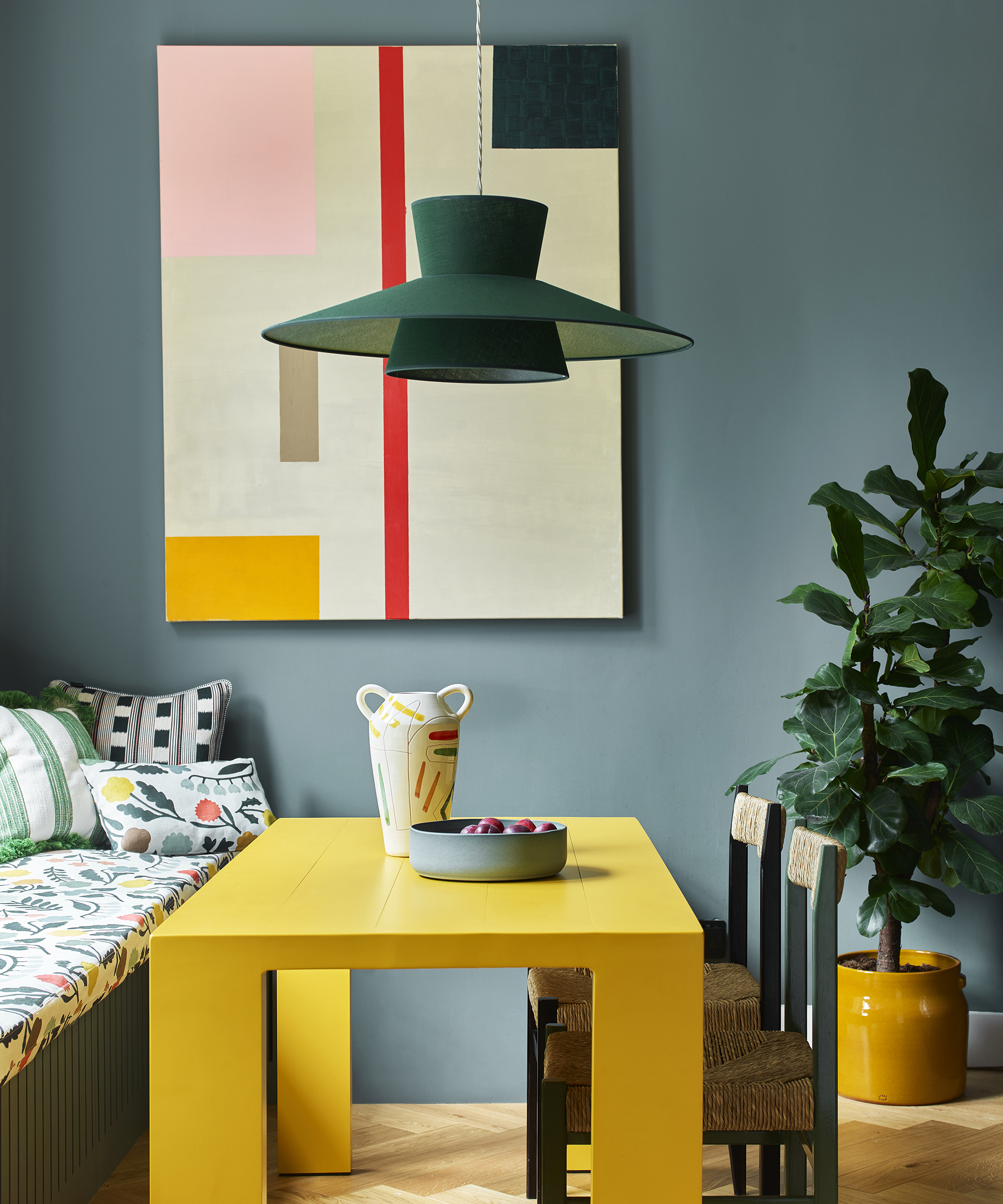 colourful kitchen dining area with yellow dining table, corner bench seating, abstract artwrork on wall and green pendant