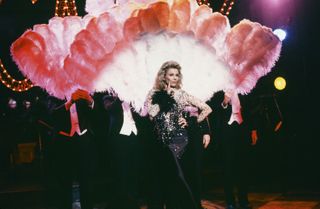 Candice Bergen wearing a gown and standing in front of feathers on an snl skit