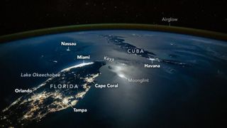 A photograph of the tip of Florida and nearby Cuba from space, with lights from cities illuminating the surface of the planet, labeled cities like Orlando and Tampa are seen as well as a green surface over Earth's labeled airglow
