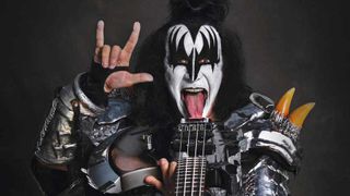 Gene Simmons in makeup throwing the horns and aiming a bass guitar at the camera
