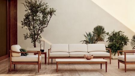 Minimalist outdoor patio set up, featuring a teak wood seating group upholstered in white Sunbrella upholstery, styled alongside lush potted plants