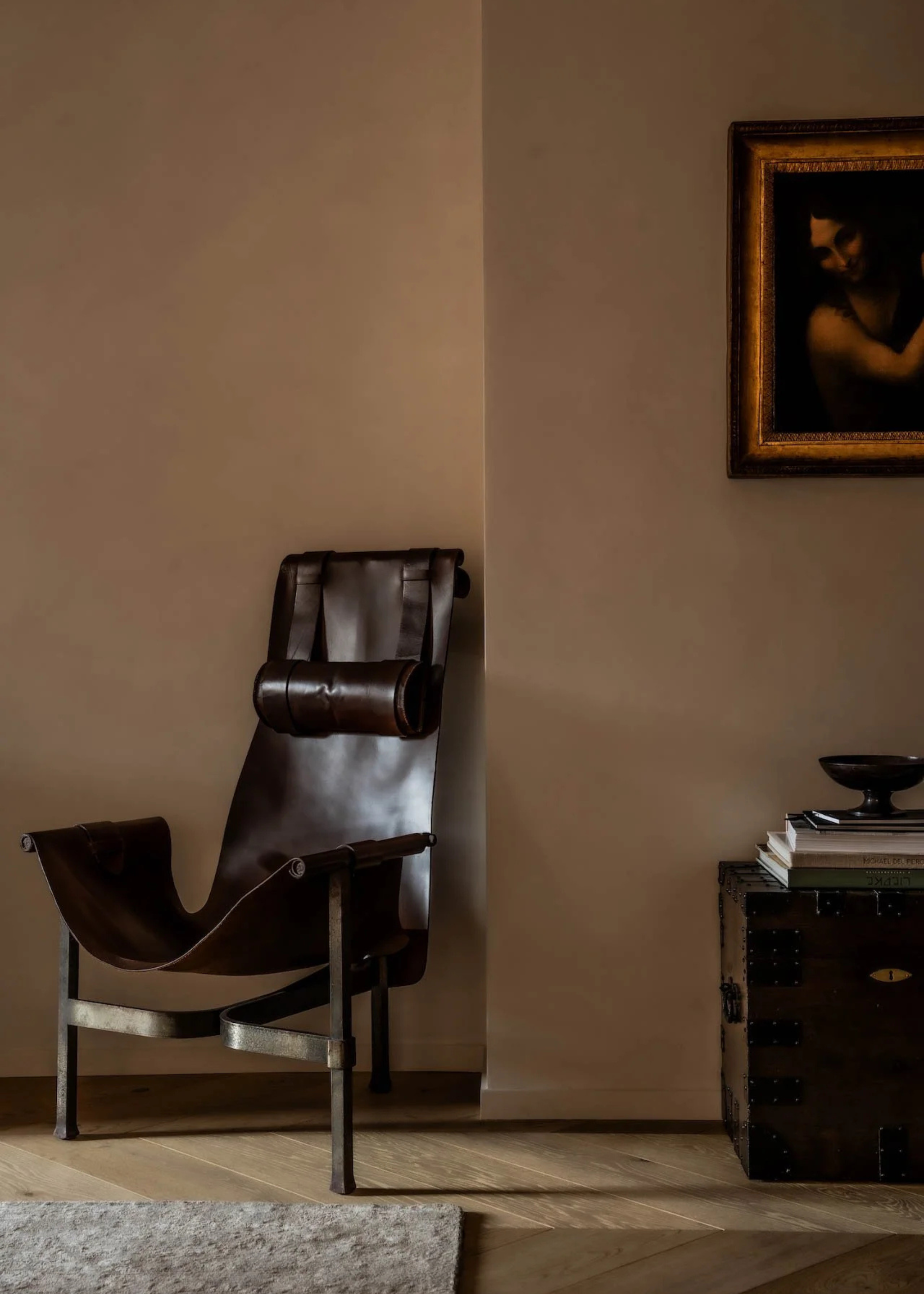 A living room corner with a leather metal chair near a sideboard with a vase and books below a framed painting