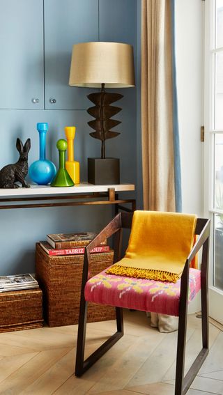 Pink and yellow flower embroidered chair with dark stained wood frame, blue walls and coloured glass vases