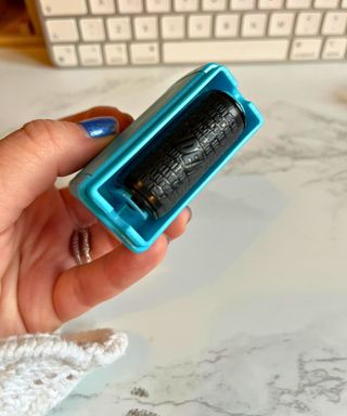 The inky underside of the stamp roller item in my hand against a marbled white and gray desk with Apple keyboard in background