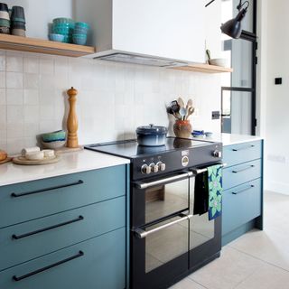 White tiled kitchen with blue painted kitchen drawers, open shelving, induction stove