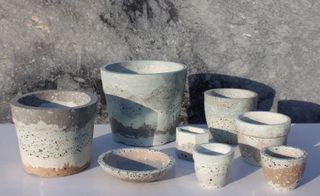 Various size stone plant pots of natural multicolours, white table top, grey concrete wall