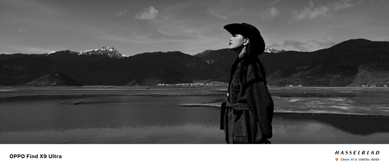 A woman in cowboy hat in front of a snowy mountain with lake, black and white