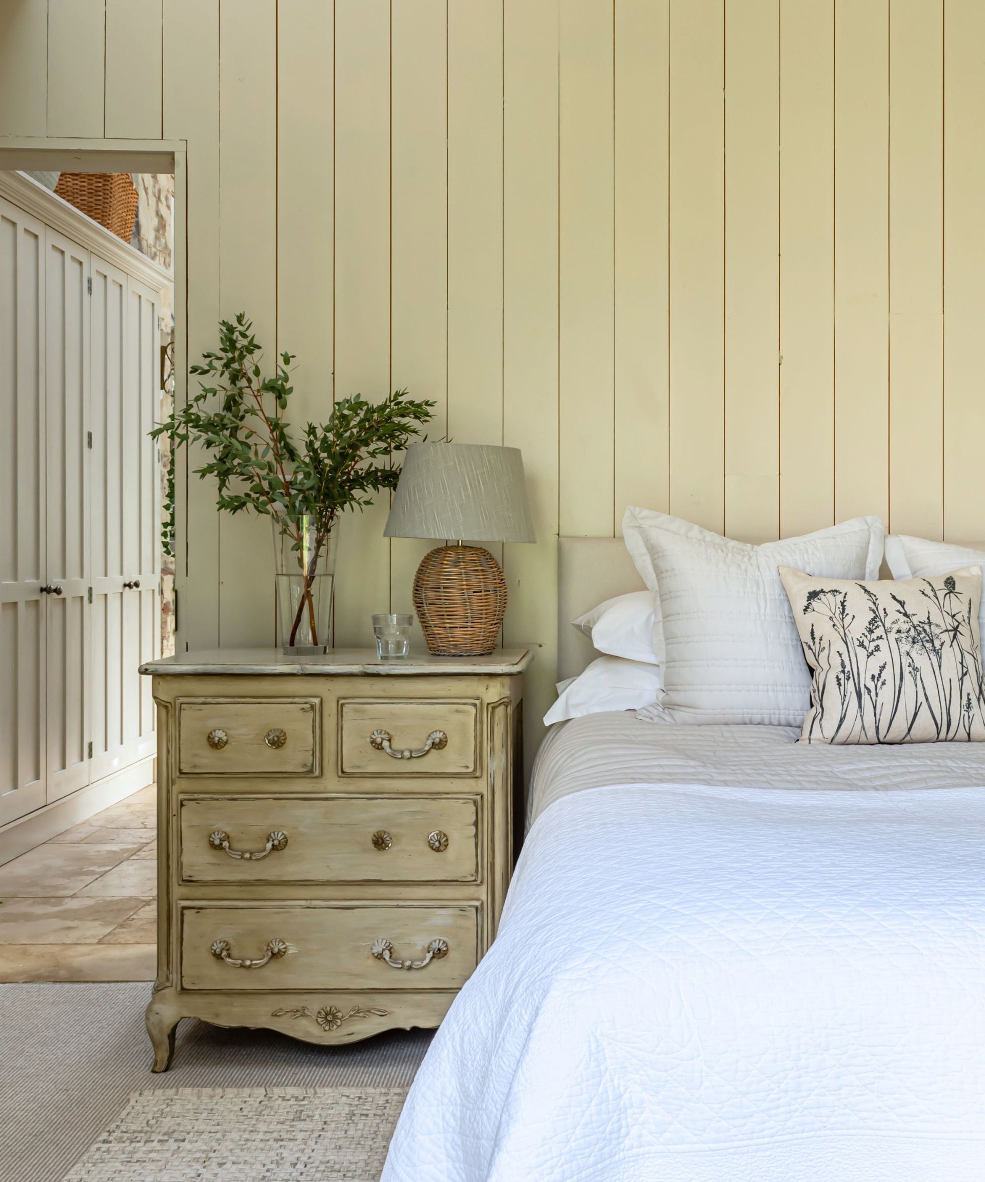 Calm neutral bedroom with paneling, white bedding and a vase of eucalyptus