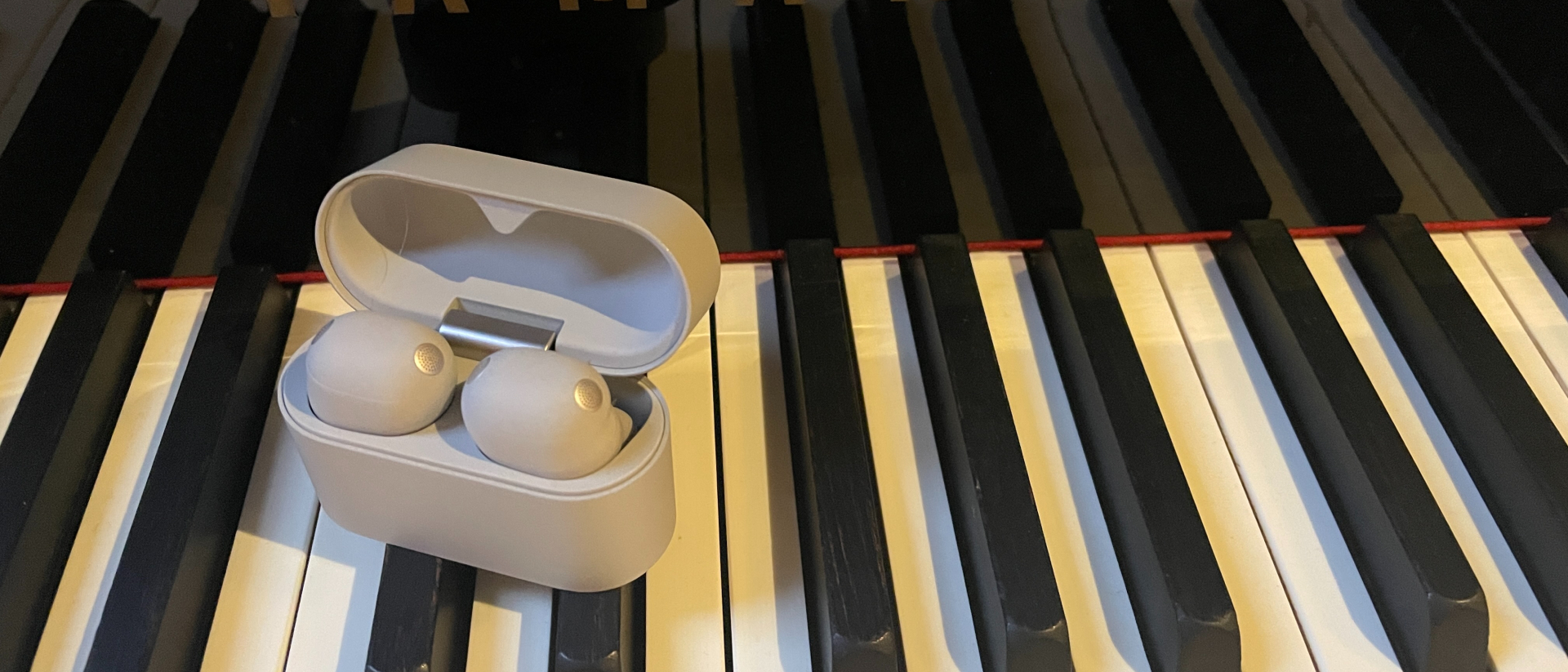 Sony WF-1000XM6 earbuds in their case, on a piano
