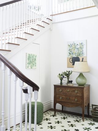 white entryway with illustrative artwork, chest of drawers, green and cream rug, lamp
