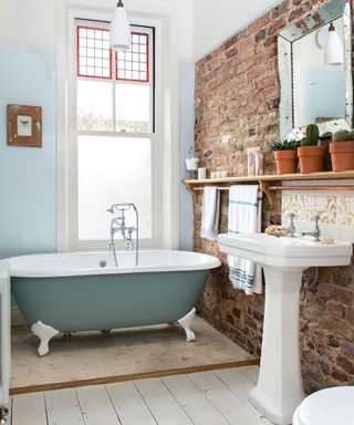 Roll top bath in bathroom with exposed brick wall and white bathroom suite