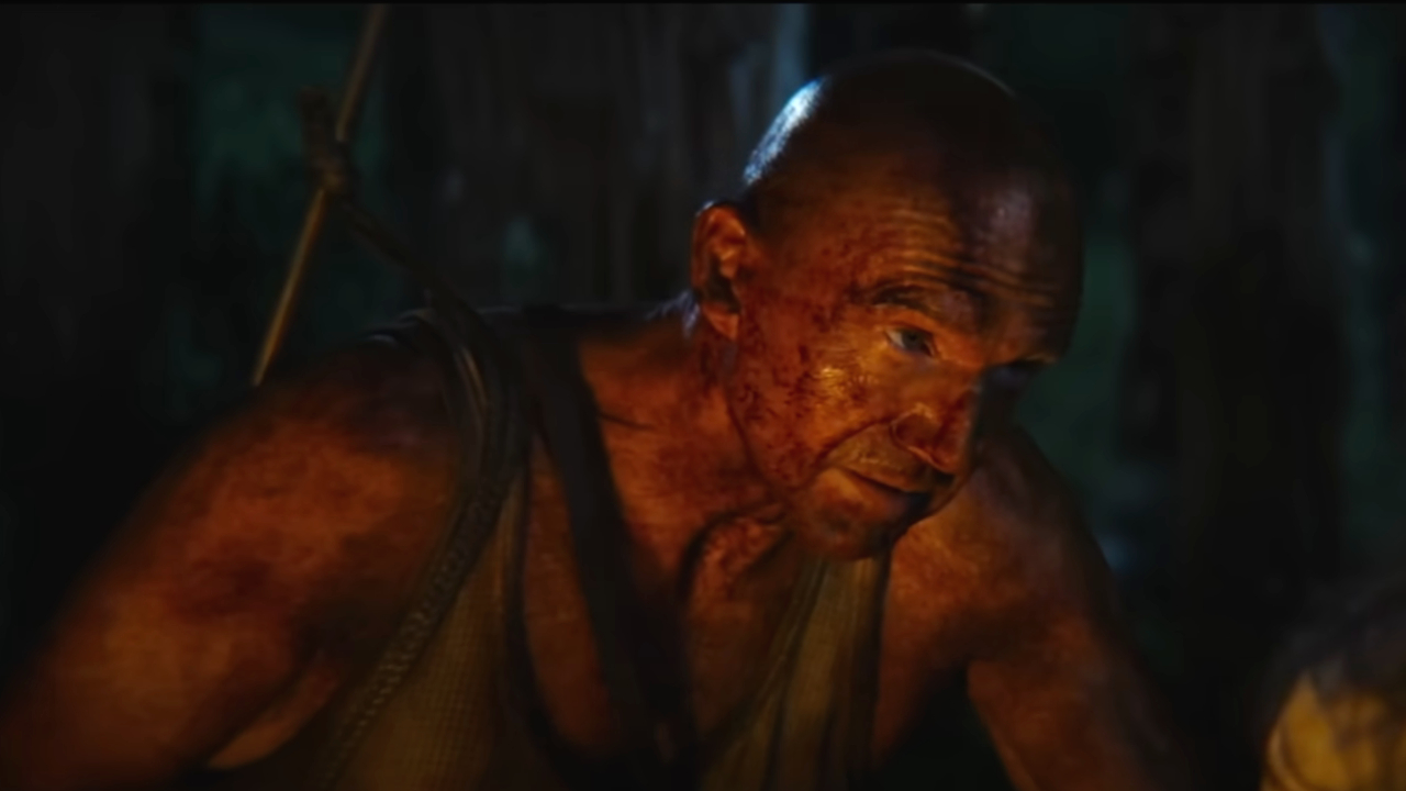 A bloodied Ralph Fiennes leans over in discussion in 28 Years Later.