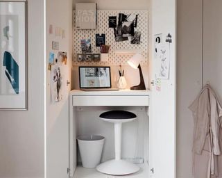 A white modern dresser with a small white desk and bench placed inside with a white pegboard