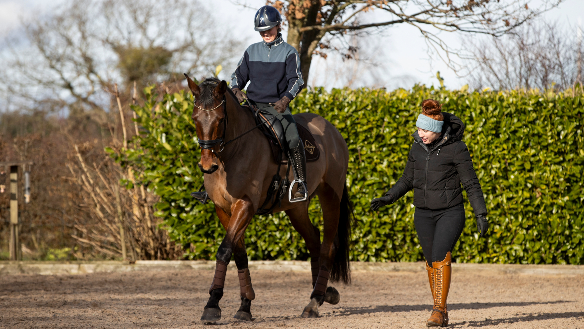 Rider riding a bay horse in walk in an outdoor arena while Becky Moody gives instructions from the ground