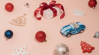 A pink paper background with Christmas baubles and Christmas tree decorations laid out on it.