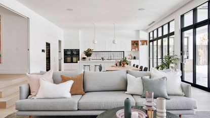 modern open plan living space with gray sofa, white kitchen and large doors out to the garden