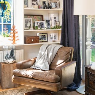 brown leather armchair and throw in cosy living room corner with framed photographs