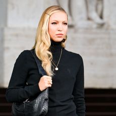 Lila wears a black turtleneck and black gucci shoulder bag.