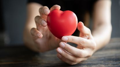 Hands hold a rounded red heart knickknack.