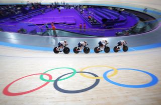 Four Japanese track cyclists ride past the Olympic rings painted on the floor of a velodrome