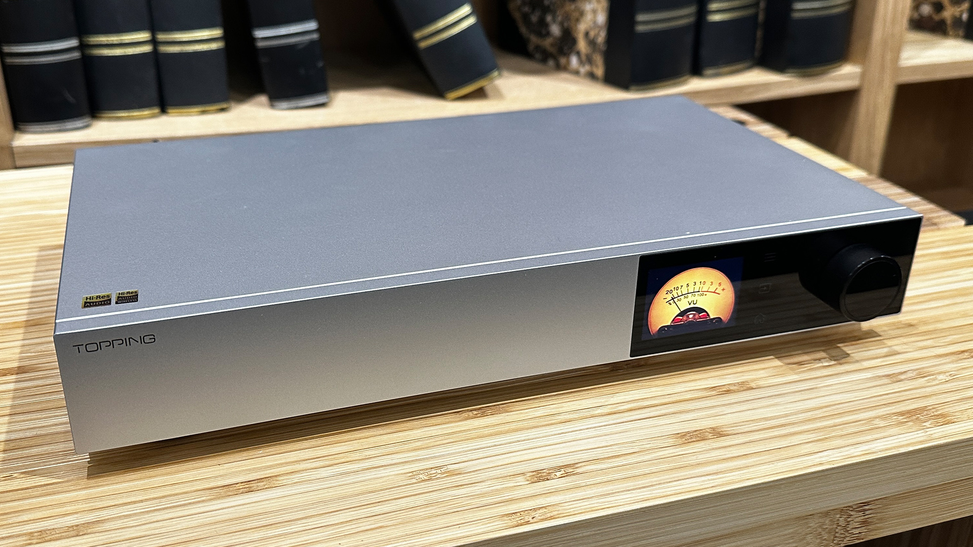 Topping Audio D900 DAC on wooden hi-fi rack in front of bookcase, on display is VU meter