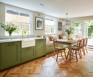 kitchen with green units, wooden herringbone flooring and built in banquette area with table and wooden chairs