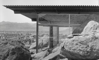 The side of a building on a rock, featuring floor to celing clear glass panels photographer in black and white