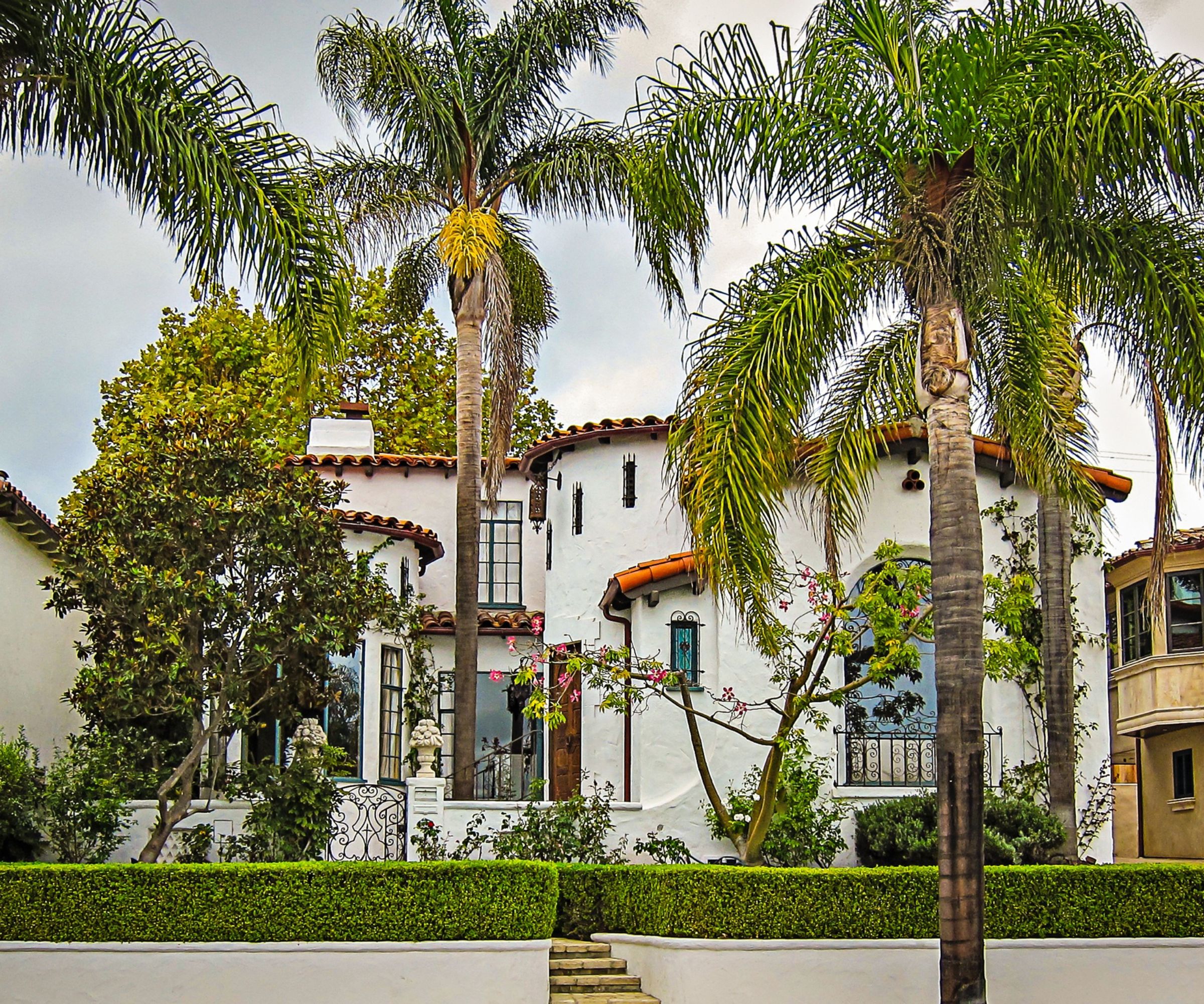 Exterior of a Tuscan-style house with a white painted facade, terracotta tiled roof and palm trees