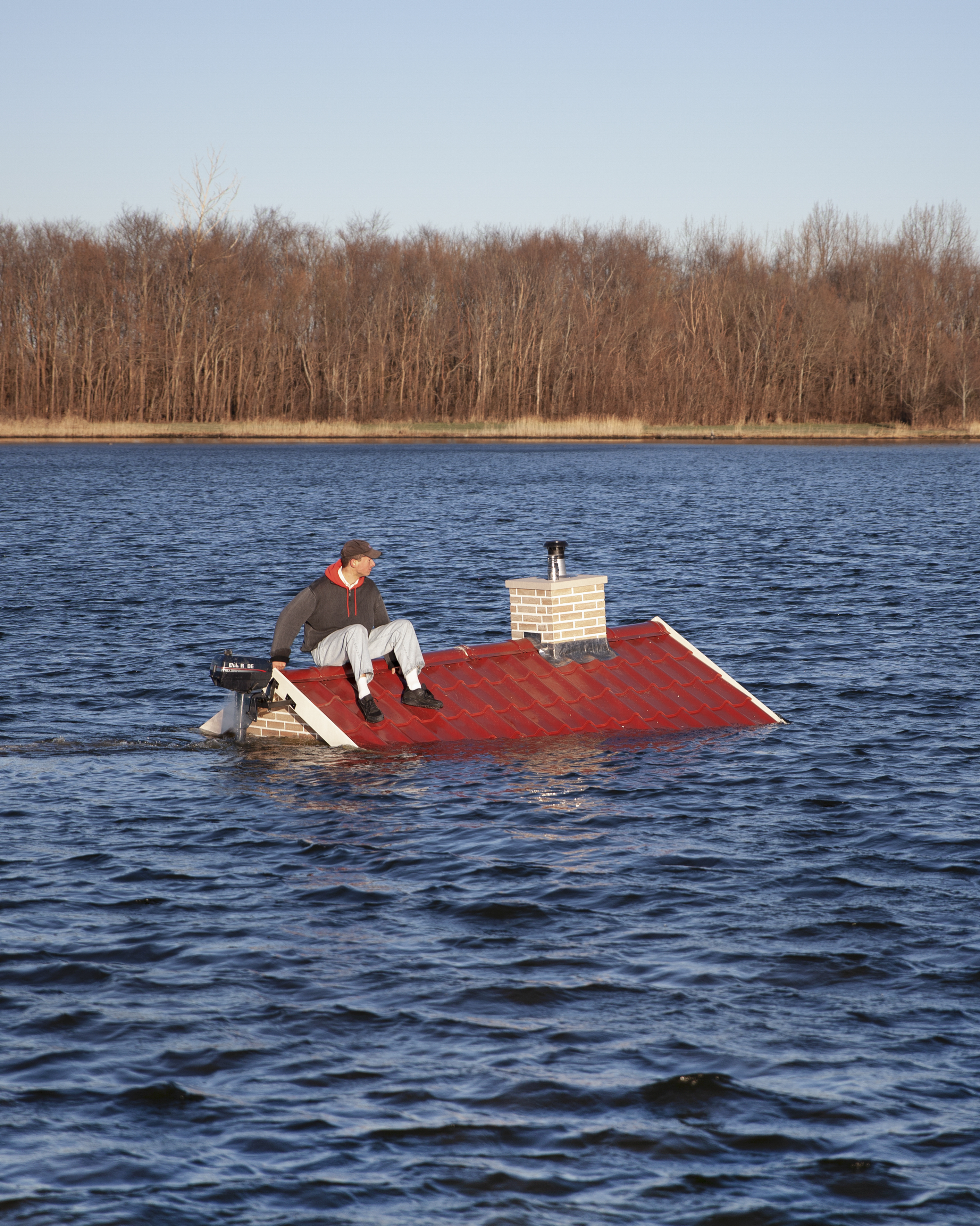 A man sitting on a red roof of a house that appears to be sinking in blue water
