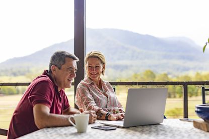 Mature couple using a laptop computer on the verandah of their farm.