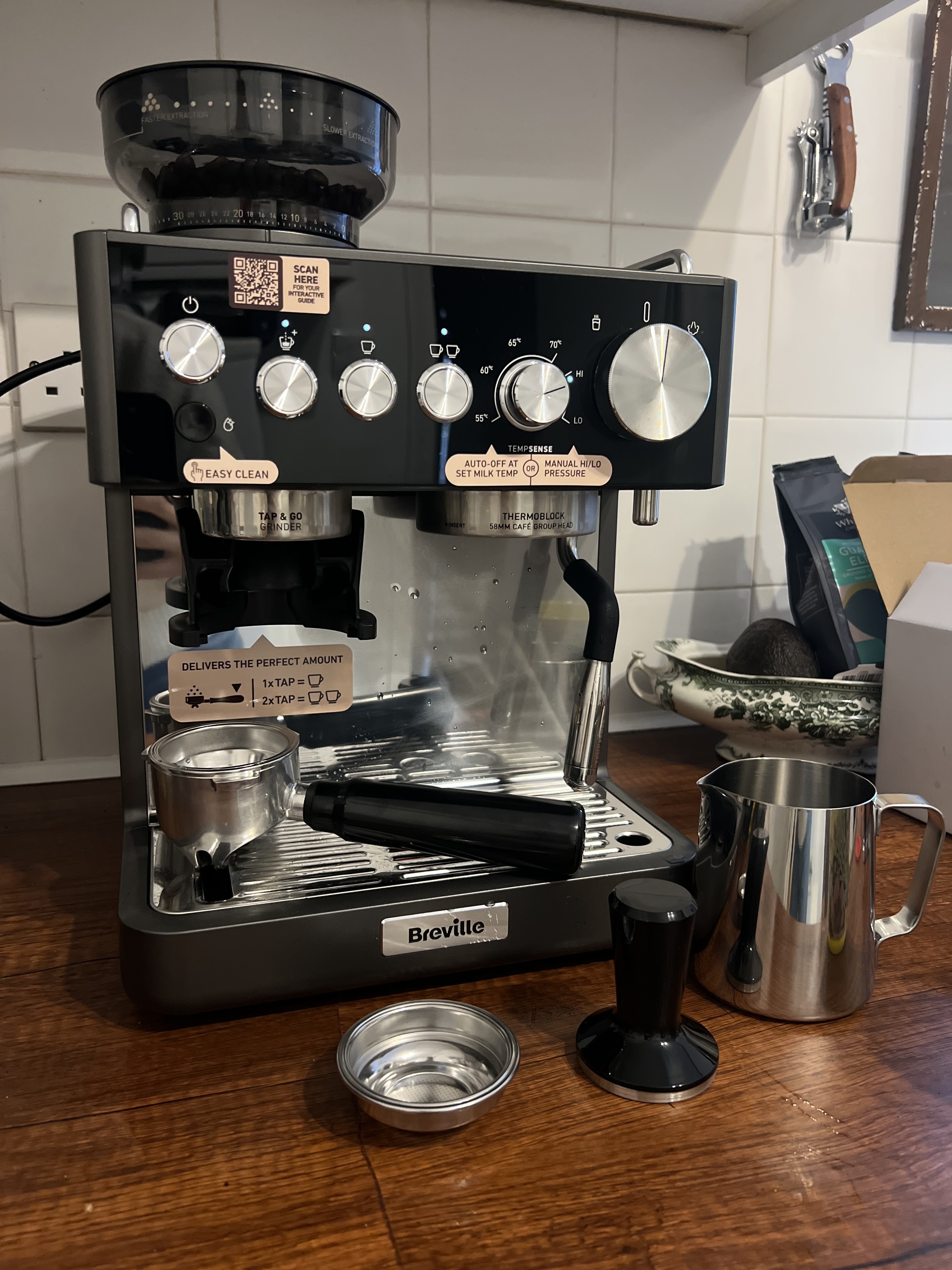 Image of the Breville Barista Sense Espresso Machine in gray and black on a wooden countertop with all of the coffee accessories around it, like the milk jug, tamper, and portafiller.