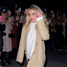 a paparazzi photo of a white woman with blonde hair waving to a crowd of people on the street