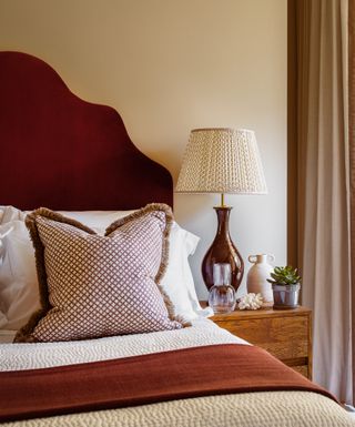 Deep red bedhead and blanket, modern wooden bedside table, brown lamp with patterned lampshade