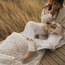 Hygge lifestyle: A woman drinking a cup of tea, wrapped up in cosy clothes and sitting on a blanket
