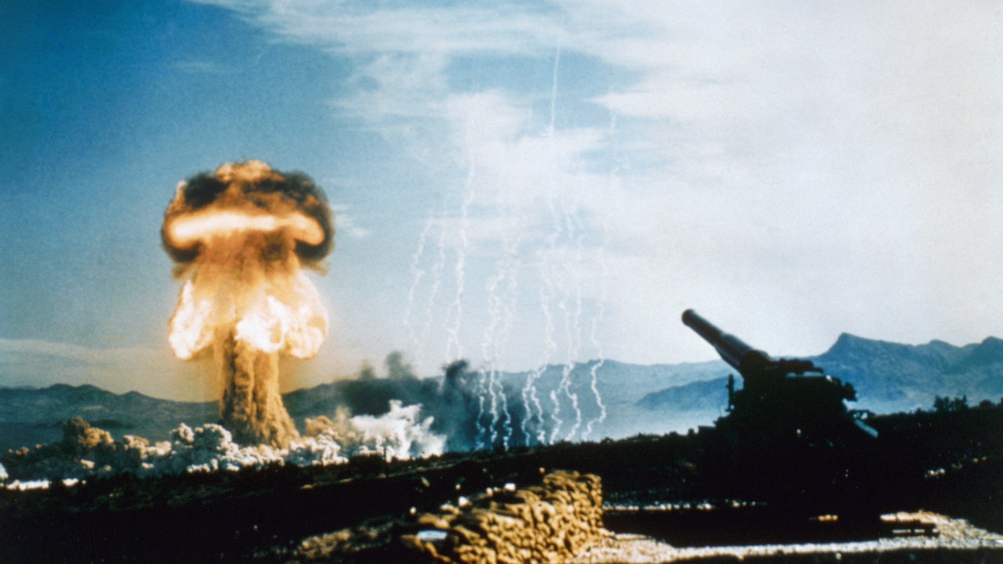 Distant nuclear detonation during a weapons test from an artillery gun pictured in the foreground