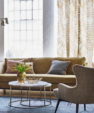 what color drapes are best for summer, living room with caramel/sand leafy patterned drapes, caramel colored couch, marble and metal round coffee table nest, blue rug, oatmeal armchair, colored cushions, vase of flowers