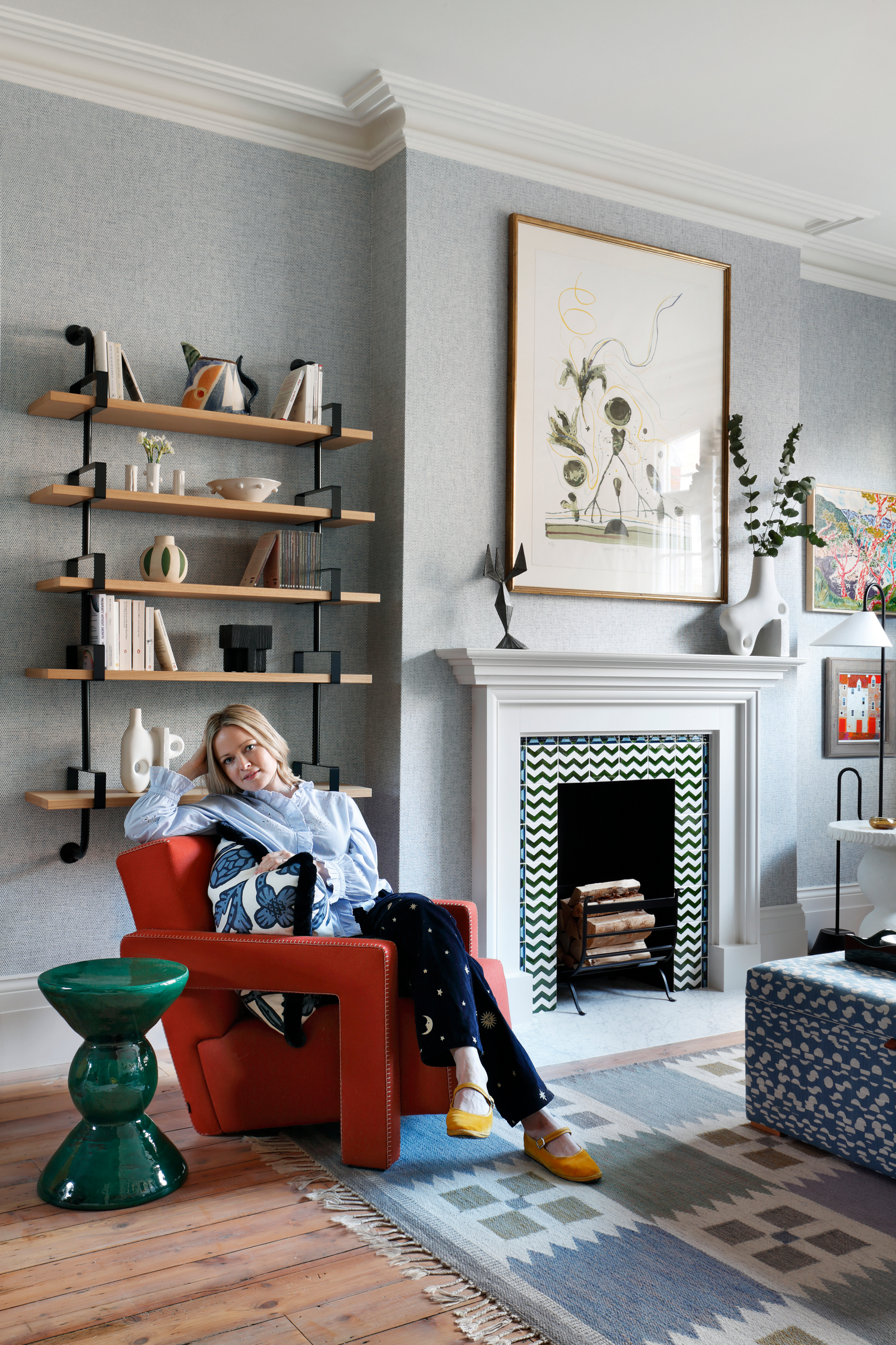 Sarah Peake pictured in a grey living room sitting on a red armchair next to a glossy green side table